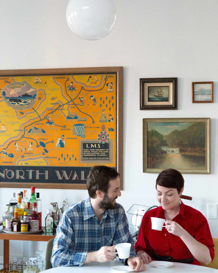 Couple enjoying coffee at a white table, with a vintage North Wales map and framed art on the wall behind them.