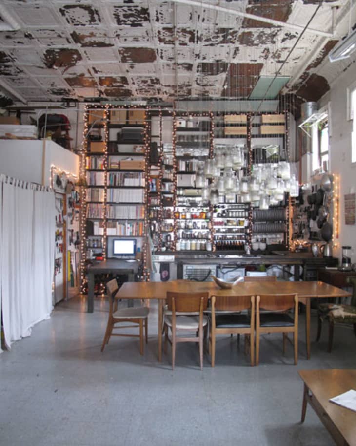 Industrial-style dining room with wooden table, chairs, exposed ceiling, and shelves filled with books and kitchenware.