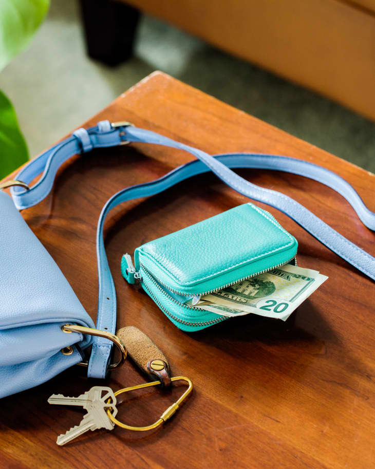 Blue purse, green wallet with some cash sticking out, and keys on a dining room table