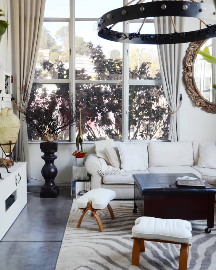 Living room with white sofa, zebra-patterned rug, large windows, and a circular chandelier.