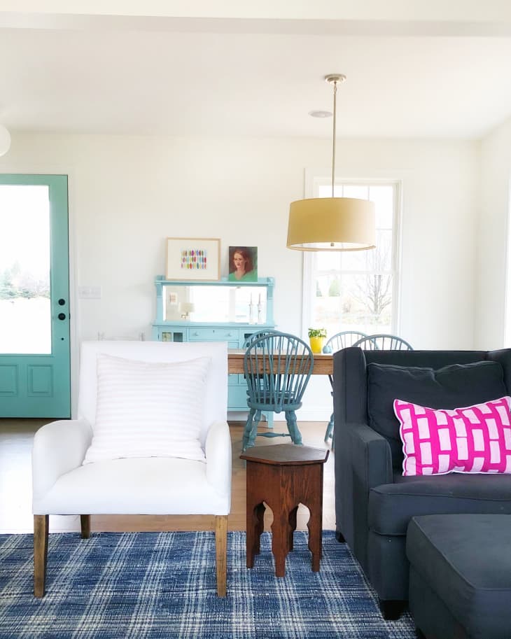 Living room with a white armchair, dark sofa, pink pillow, blue checkered rug, and turquoise door.