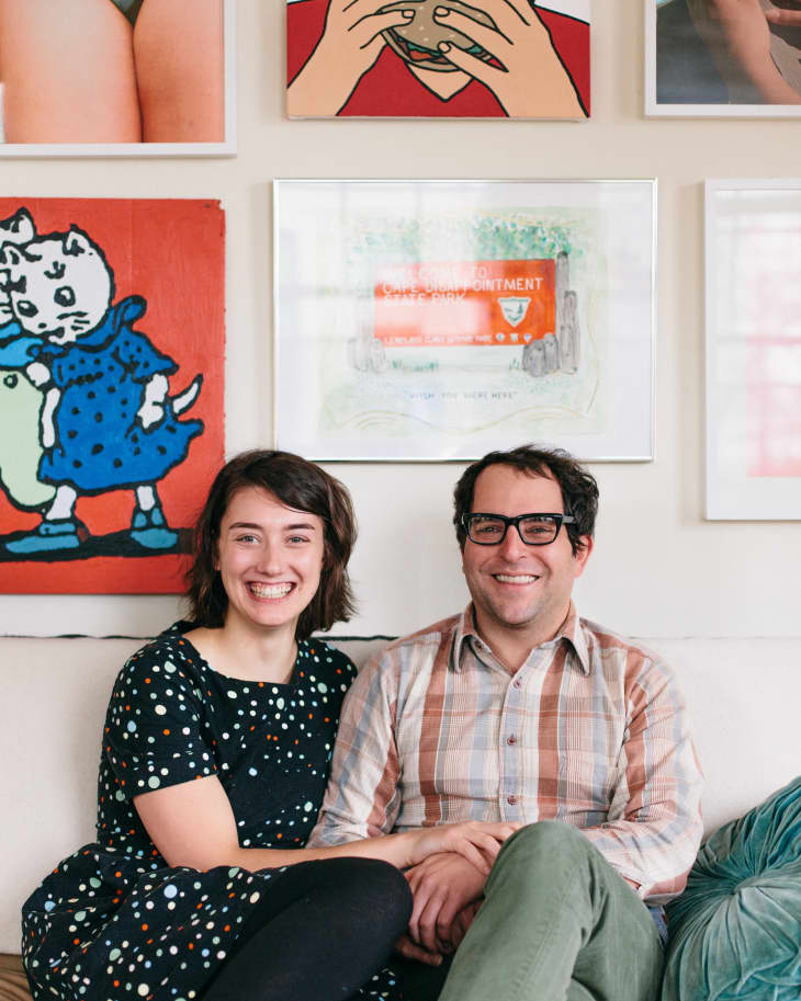 Couple sitting on a sofa in front of a gallery wall with colorful artwork.