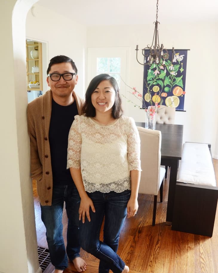 Couple standing in a dining room with a dark wood table, chandelier, and colorful wall art.