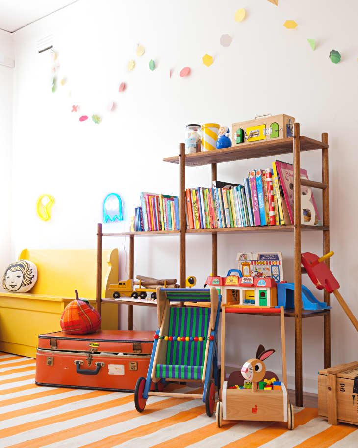 Colorful children's playroom with books, toys, a striped rug, and a wooden shelf.