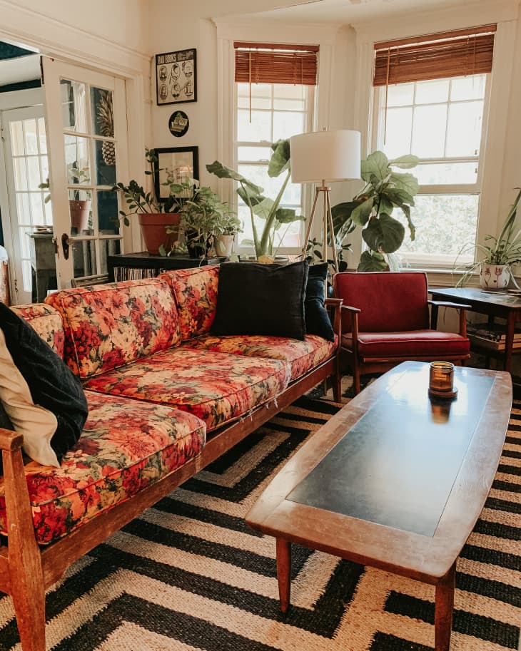 Living room with floral sofa, red chair, wooden coffee table, and large potted plants by the window.