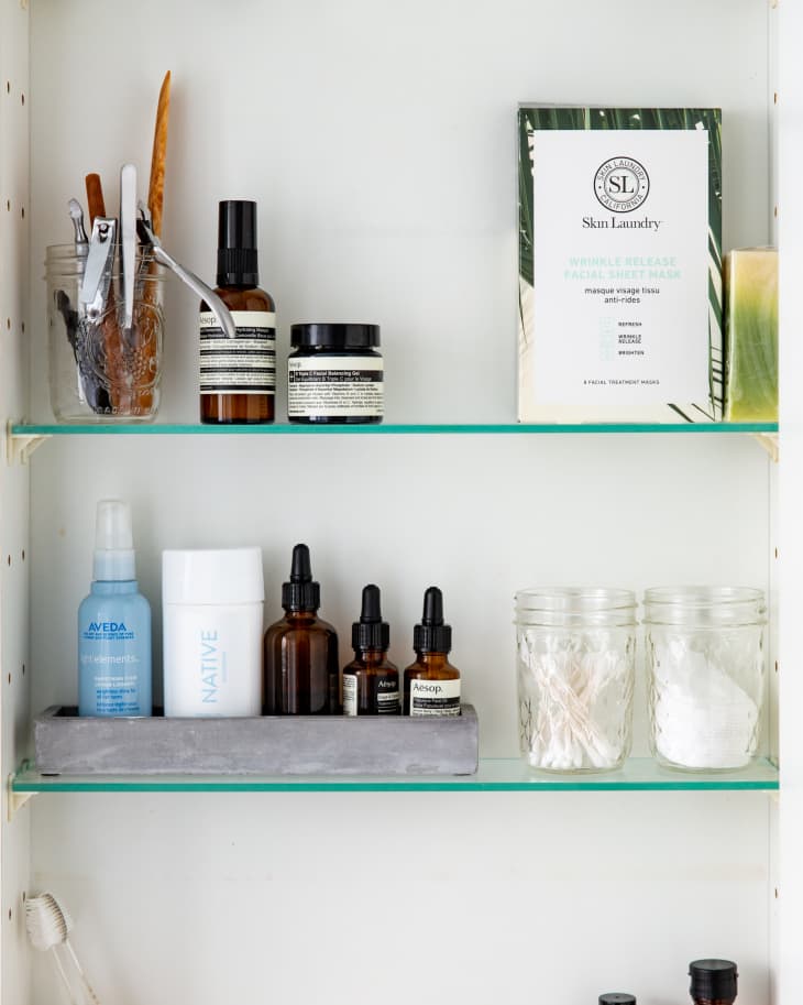 Bathroom shelf with skincare products, glass jars, cotton swabs, and a toothbrush in a holder.