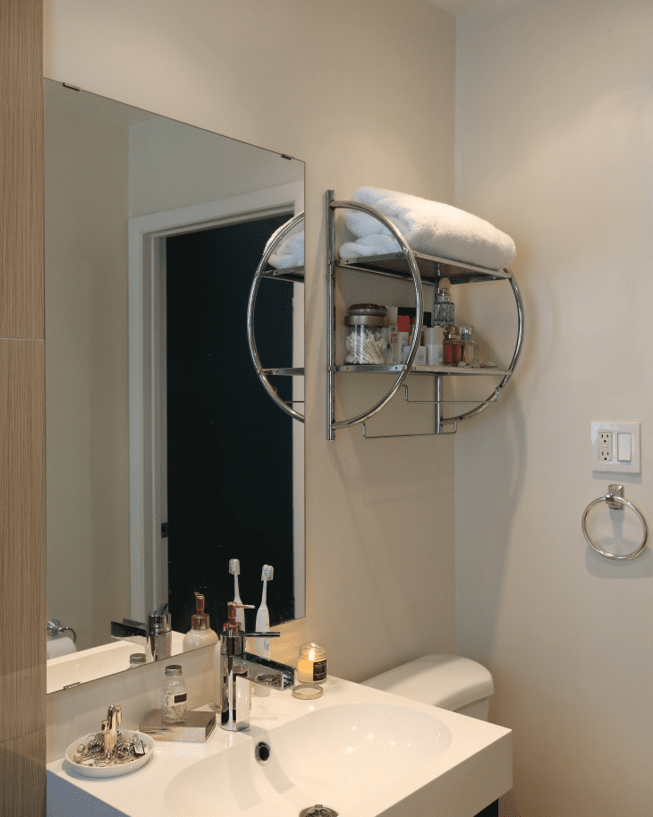 Small bathroom with a white sink, large mirror, chrome shelf holding towels and toiletries, and a candle.