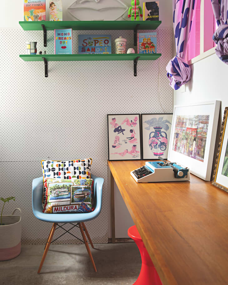 Colorful home office with a blue chair, patterned pillows, green shelves with books, and a wooden desk with a typewriter.