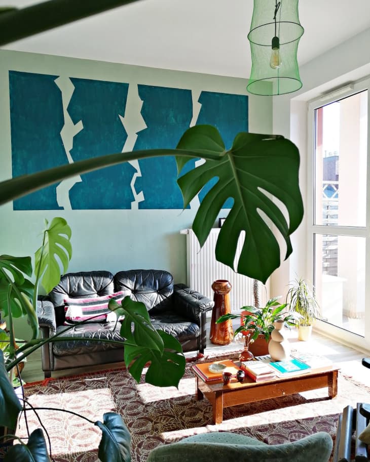 Living room with black leather sofa, large green plant, wooden coffee table, abstract blue wall art, and a green pendant light.