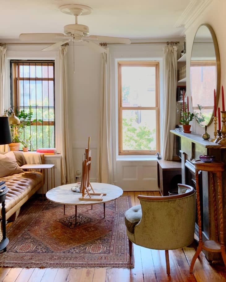 Cozy living room with a tufted sofa, round marble table, green chair, and large mirror above a fireplace.