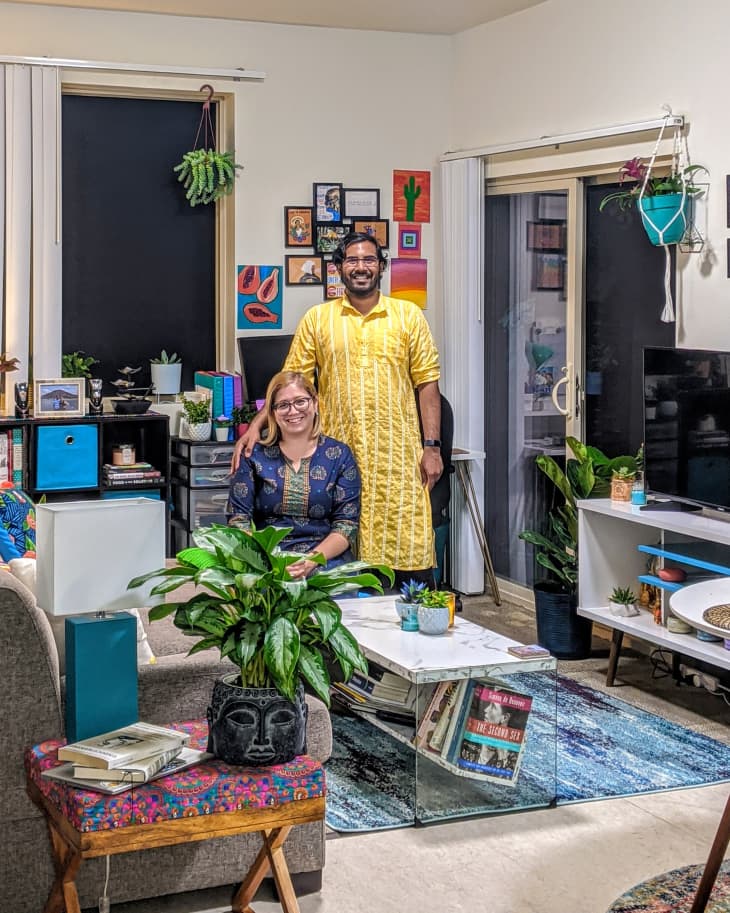 Couple in a colorful living room with plants, books, and wall art, sitting on a sofa near a glass coffee table.