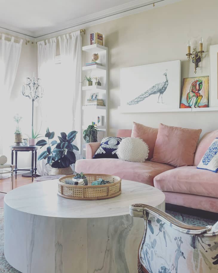 Living room with pink sofa, round marble table, plants, and colorful artwork on the wall.