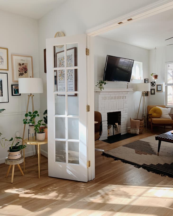 French doors open to a cozy living room with a white brick fireplace, wall art, plants, and a mounted TV.