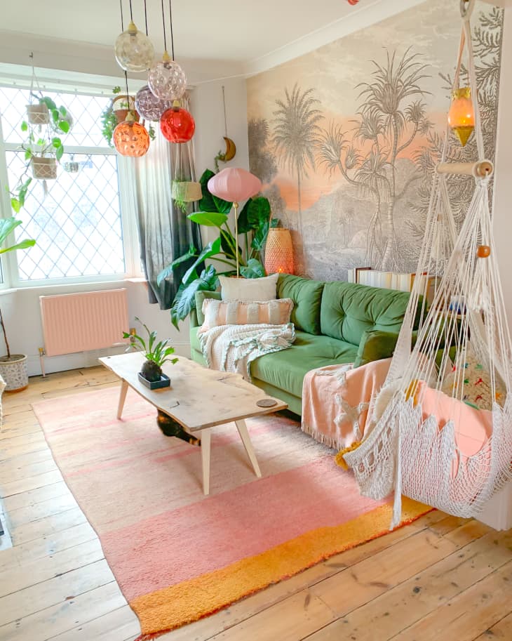 Colorful bohemian plant-filled living room with green sofa and chair hammock