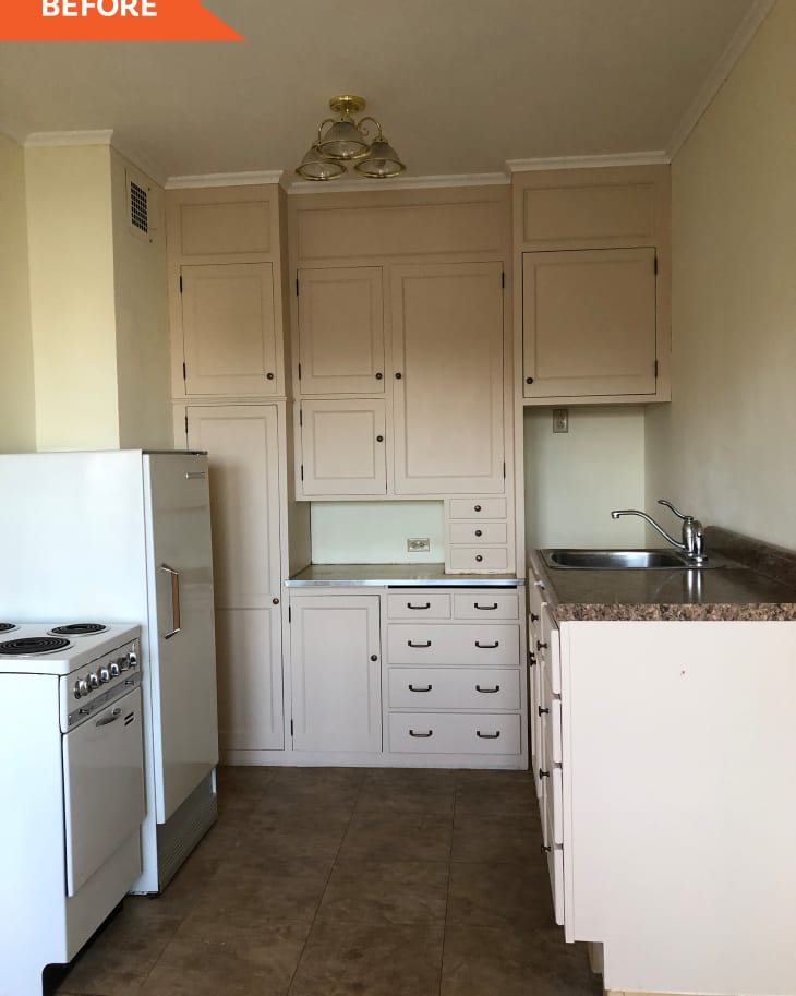 Small kitchen with beige cabinets, white stove, and fridge, brown countertop, and tiled floor under a brass light fixture.