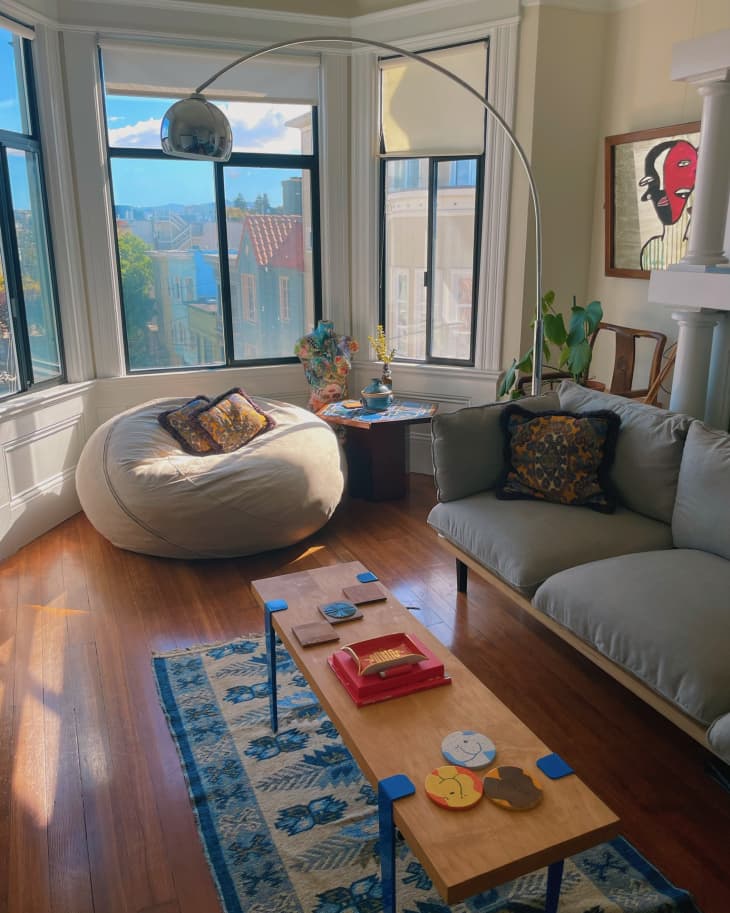 A living room with bay windows, a gray couch, and a large bean bag
