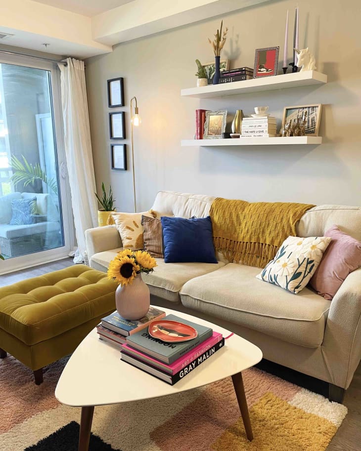 A white couch with a yellow ottoman on top of a pink, yellow, white, and blue rug