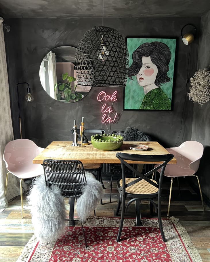 dining room with gray sueded walls, pale pink dining chairs, black metal accents, framed painted portrait, pink neon saying "ooh la la", pendant lamp with black basket/netting shade