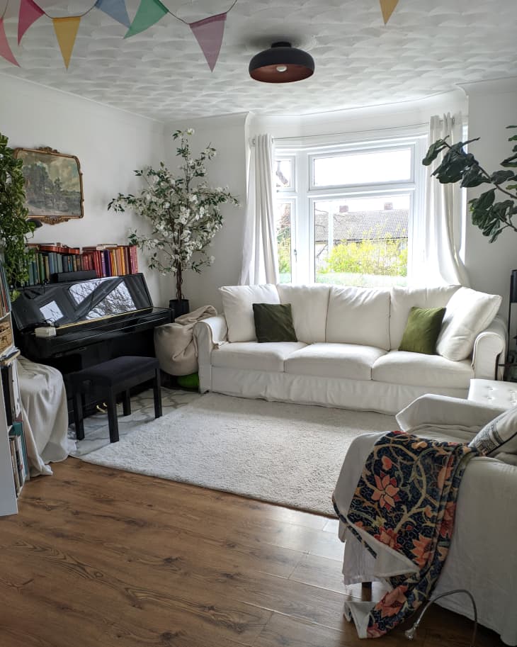 Light filled living room with white comfortable furniture and colorful bunting on the ceiling.