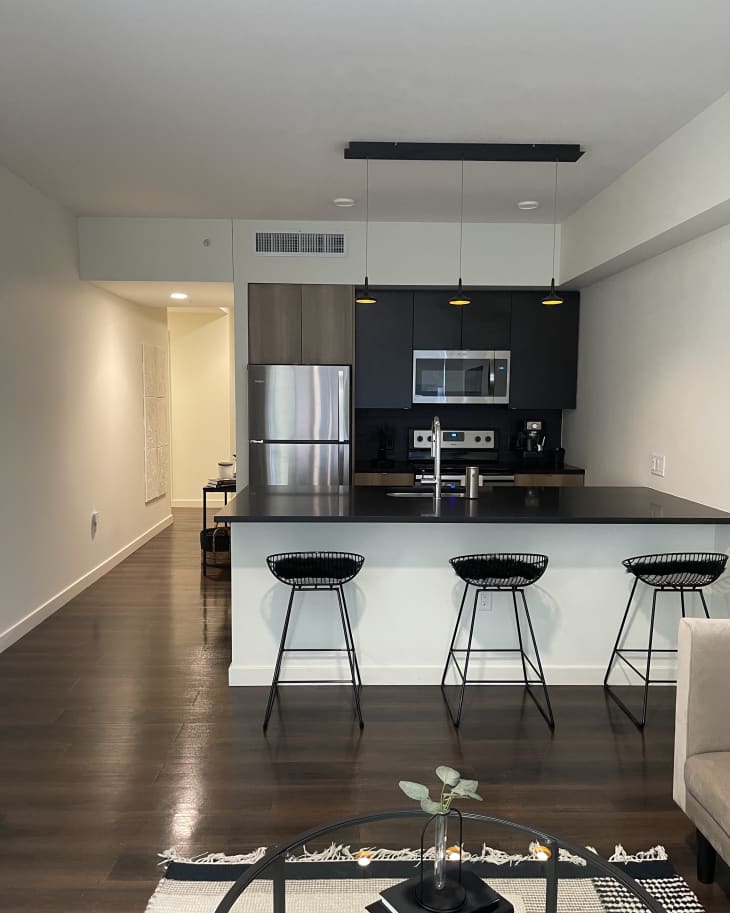 Modern kitchen with black countertops, stainless steel appliances, and three black wire bar stools at the island.