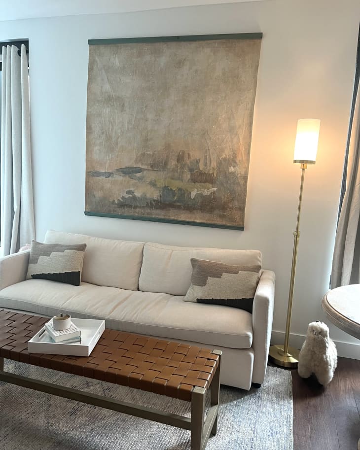 white walls, beige impressionist abstract painting, long wood slated coffee table, beige rug, wood floors, white couch