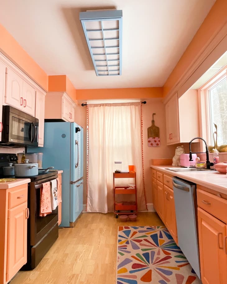 kitchen, blue refrigerator, blue dishwasher, peach cabinets, wood floors, blue florescent light, floral runner, blue pots