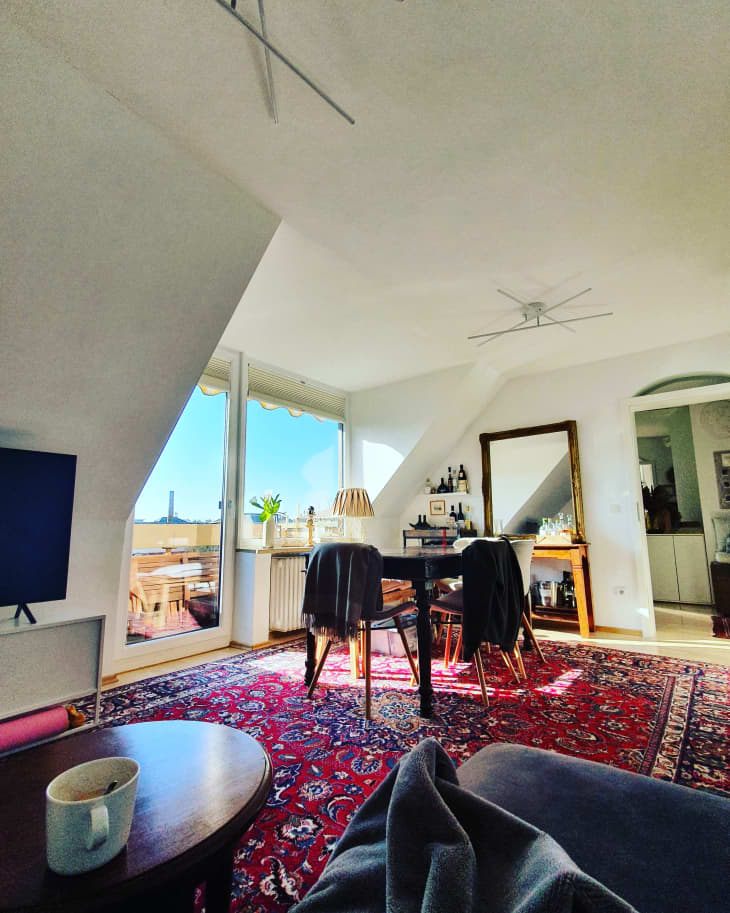Living room with red and blue rug and large windows in city apartment.