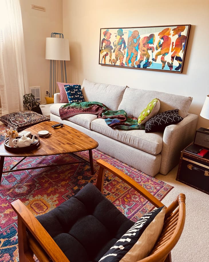 A painting hanging above a pillow-filled gray couch next to a wooden coffee table and colorful rug