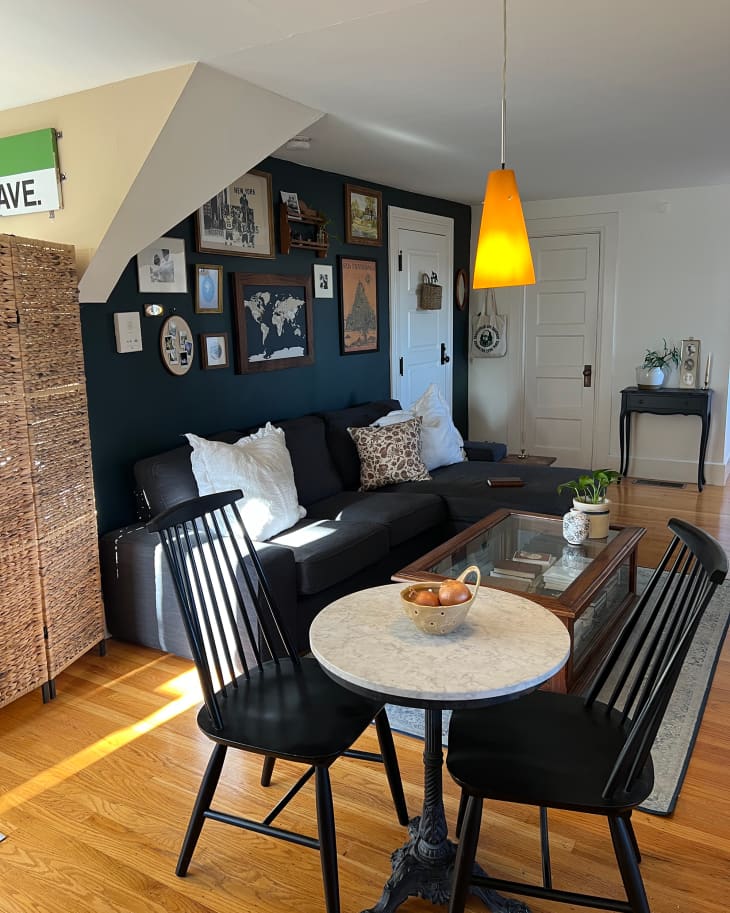 Orange and yellow pendant light above bistro table surrounded by two black dining chairs in studio apartment.
