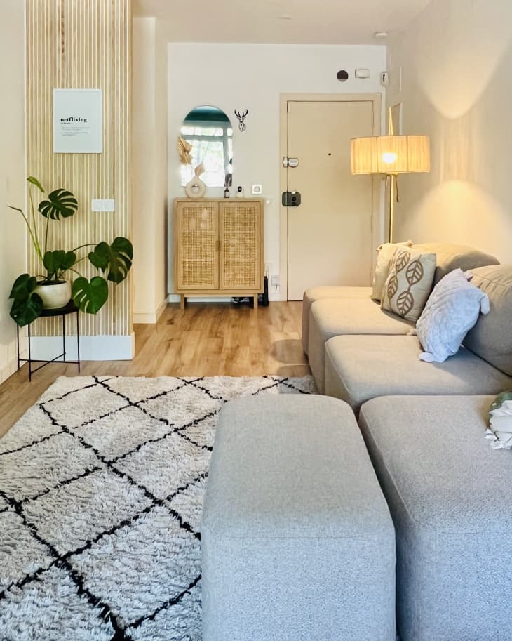 beige and black diamond pattern rug with beige sectional couch and light wood paneling on portion of wall