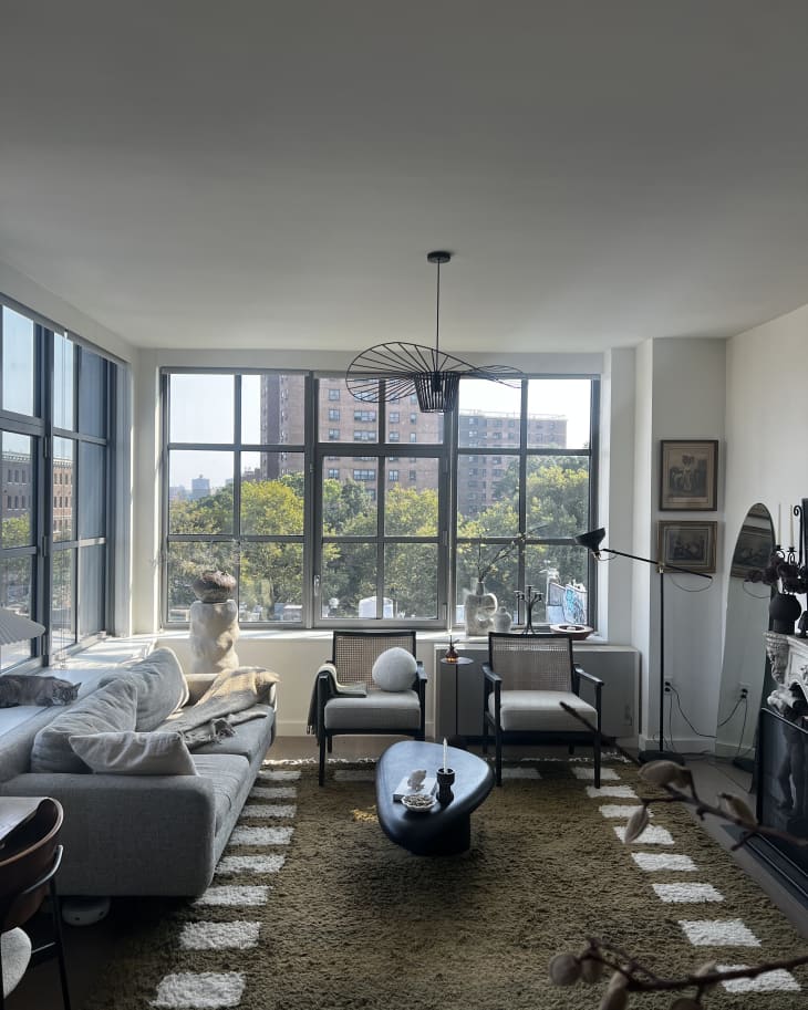 floor to ceiling square paneled windows, grey couch, two white matching arm chairs, green and white geometric outline rug