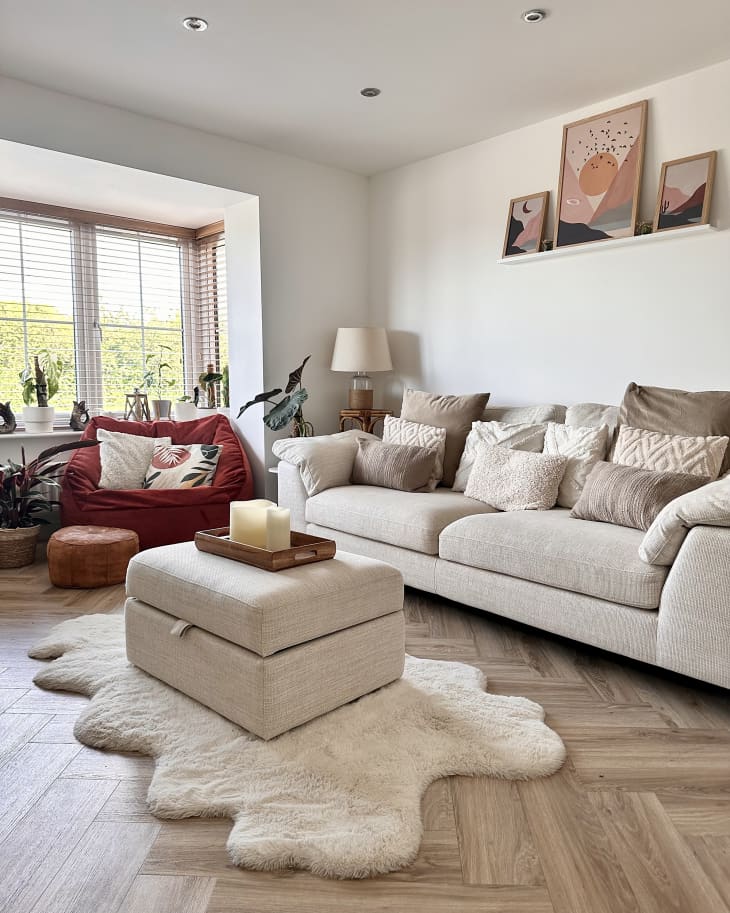 White living room with pale neutral sofa, brick red velvet cozy chair, and lots of throw pillows
