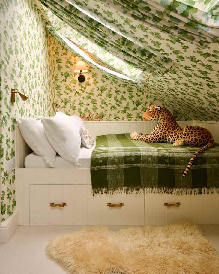 Cozy attic bedroom with green leaf-patterned wallpaper, a bed with white pillows, a green throw, and a plush leopard toy.