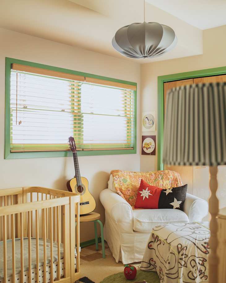 Cozy nursery with a wooden crib, white armchair, colorful pillows, guitar, and playful decor.