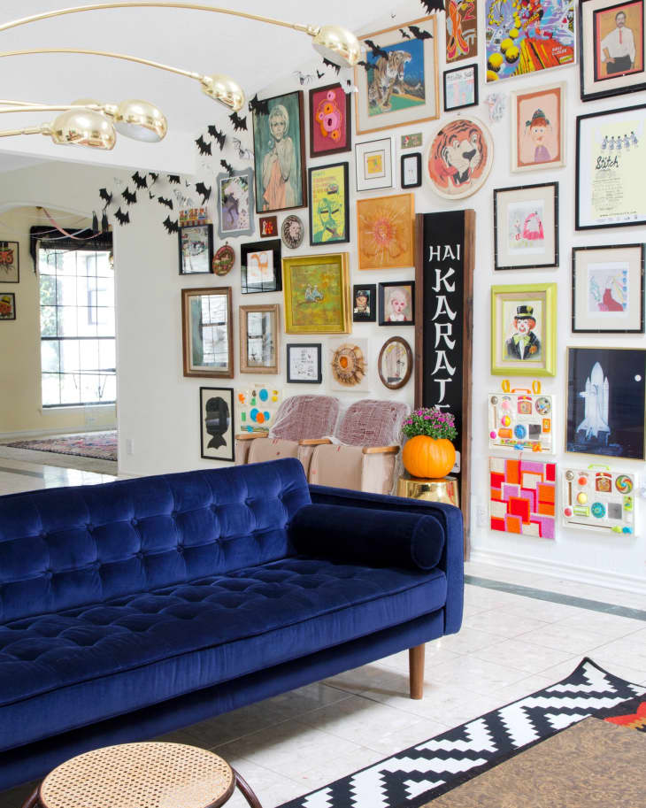 Blue velvet sofa in a living room with eclectic gallery wall, gold light fixture, and Halloween bat decorations.