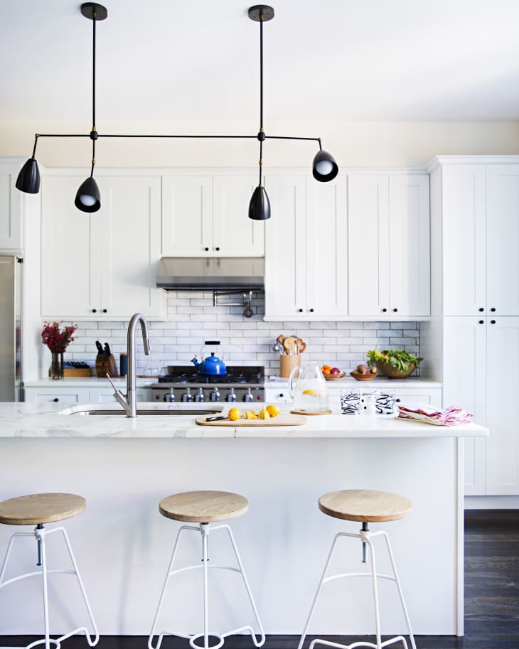 Modern kitchen with white cabinets, island with wooden stools, pendant lights, and a blue kettle on the stove.