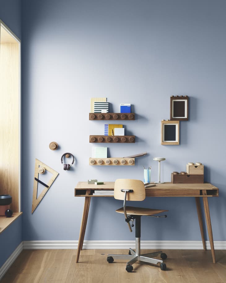 Mid-century modern desk with wooden chair, wall shelves, geometric decor, and a lamp in a blue-walled room.