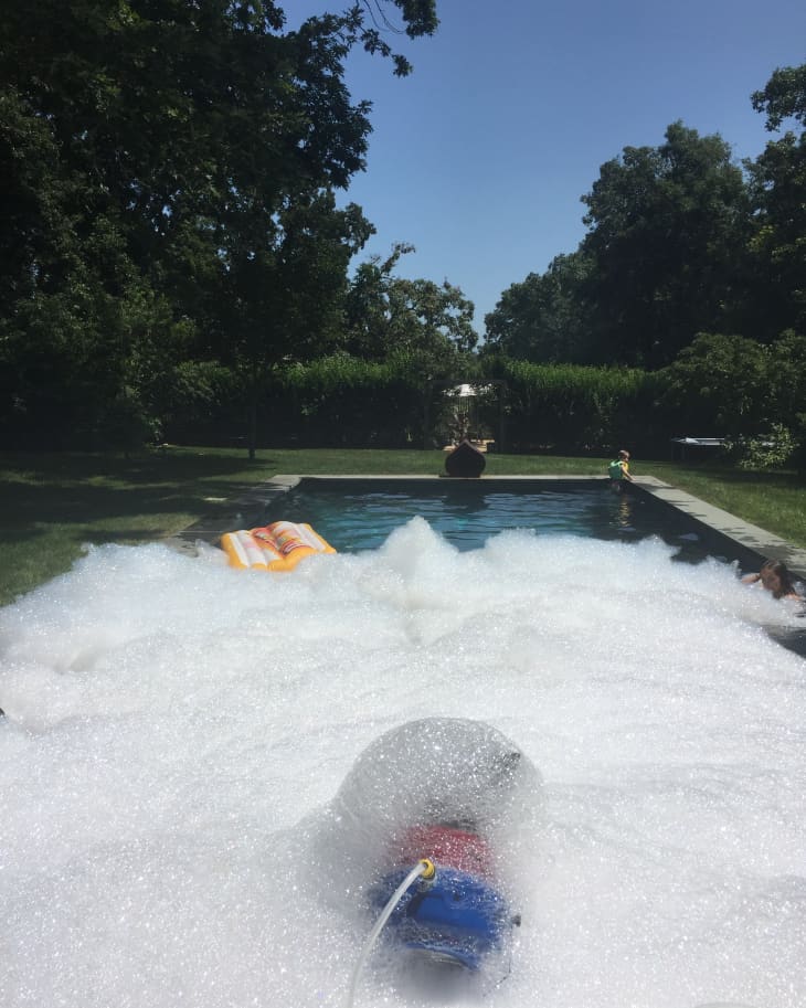 Foam-filled pool with a person swimming, surrounded by trees and a clear blue sky.