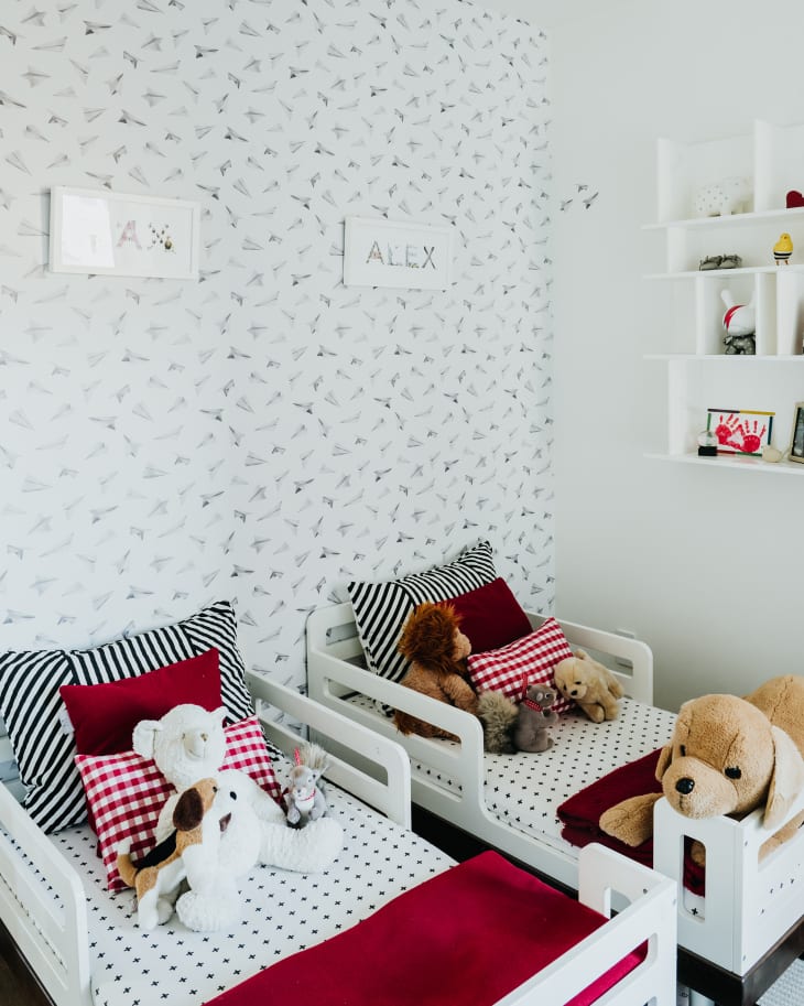 Boys' bedroom in NYC. Lots of white, white walls, white shelves, white furniture, with pops of color: red bed linens, patterned throw pillows, etc