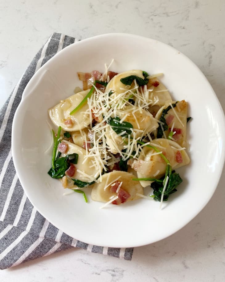 Pierogi with spinach, bacon, and grated cheese on a white plate with a striped napkin.