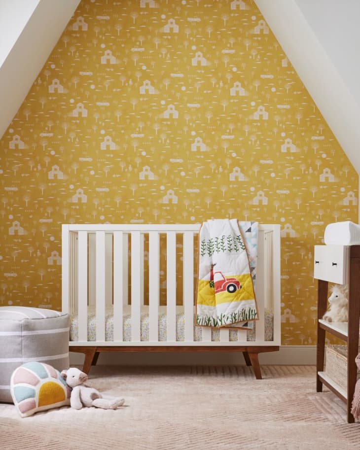 Nursery with a white crib, yellow patterned wallpaper, changing table, and colorful quilt featuring a red tractor.