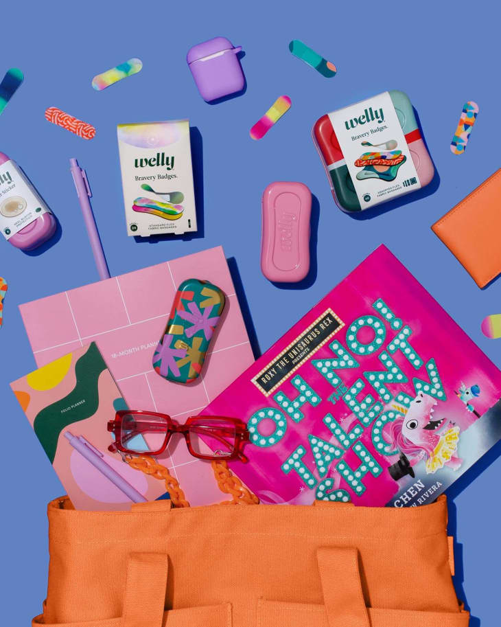 Orange tote with planner, pink book, colorful bandages, glasses, and wallet on a blue background.