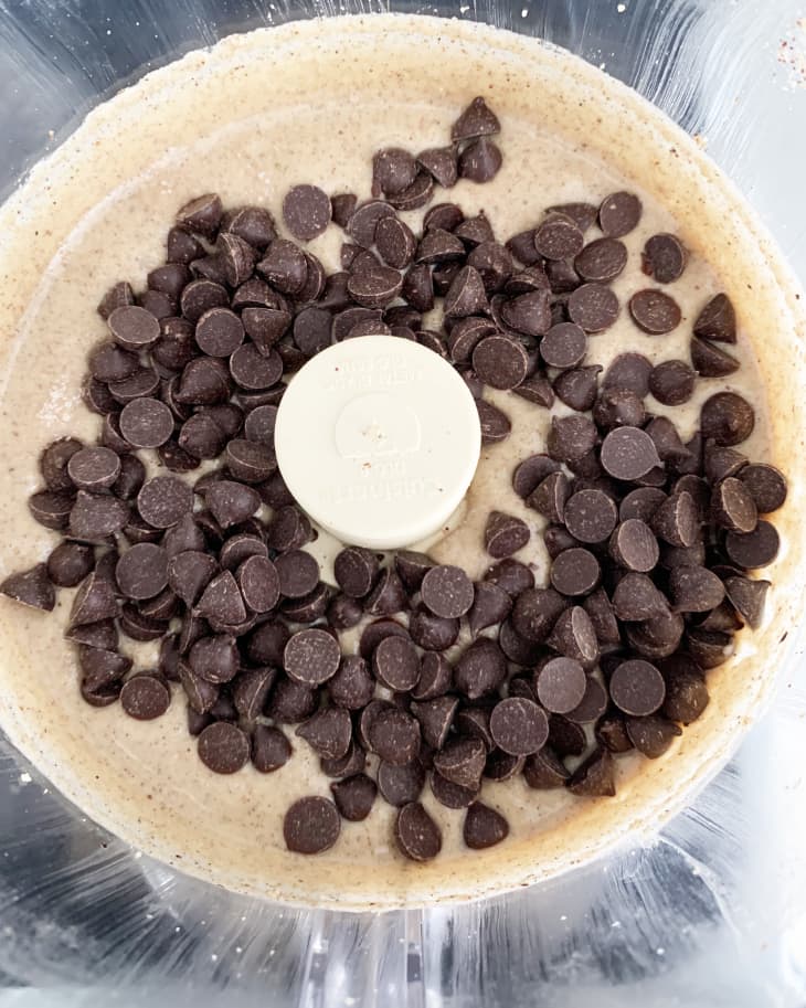 Chocolate chips on creamy batter in a food processor bowl.
