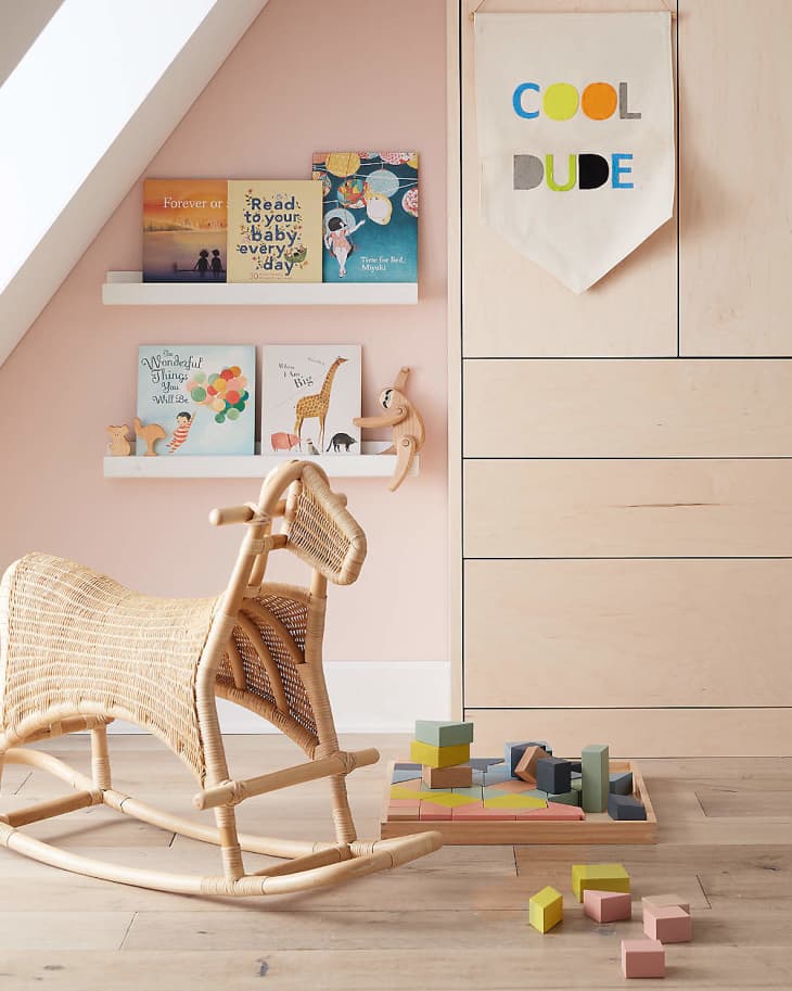 Children's room with wicker rocking horse, books on shelves, colorful blocks, and a "Cool Dude" banner on the wall.