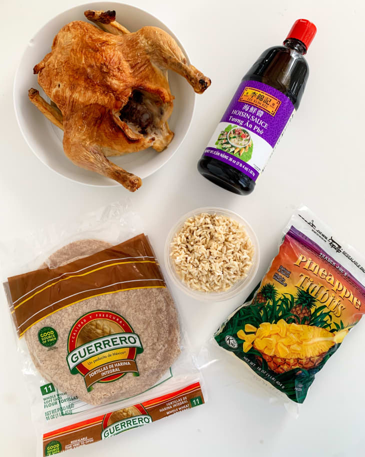 Whole roasted chicken, hoisin sauce, whole wheat tortillas, cooked rice, and pineapple tidbits on a white surface.