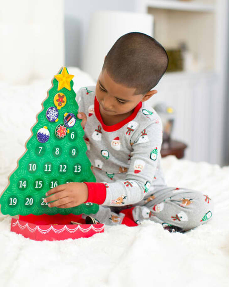 Little boy sitting on bed in pajamas, hanging ornaments on a Christmas tree advent calendar