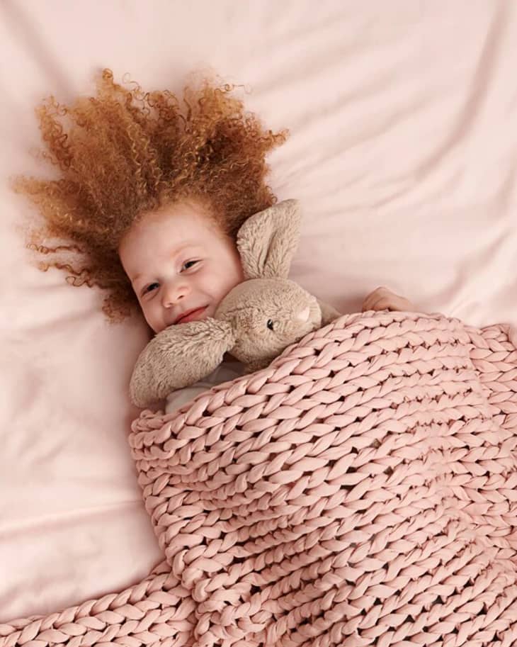 little girl wrapped in rose weighted blanket on rose sheets