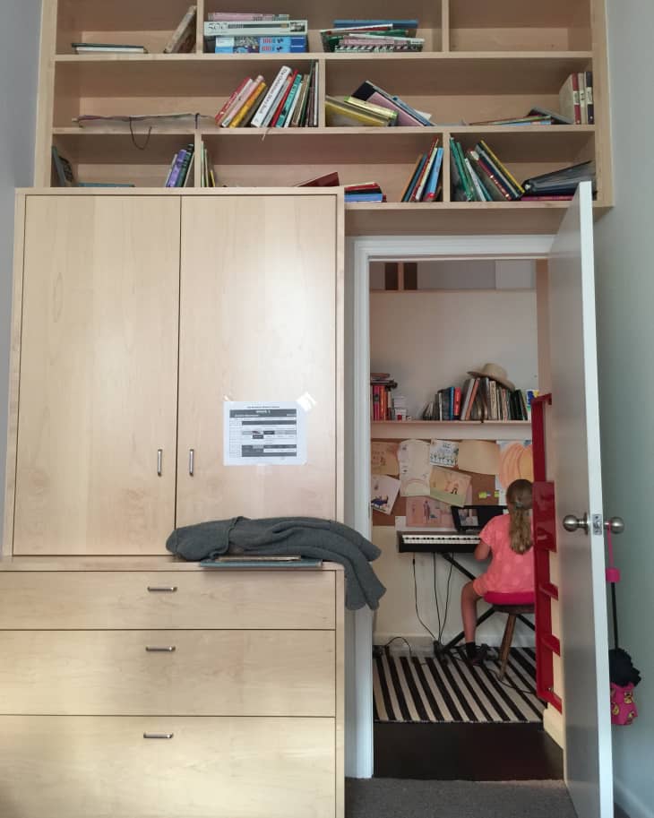 Child playing keyboard in a small room with bookshelves, wooden cabinet, and striped rug.