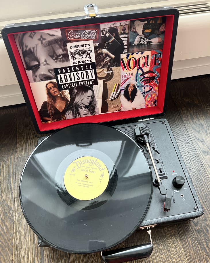 Open black record player with a vinyl disc, surrounded by a collage of magazine cutouts and stickers.