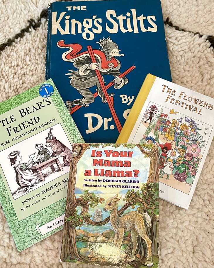 Four children's books on a textured rug: "The King's Stilts," "Little Bear's Friend," "Is Your Mama a Llama?," and "The Flowers' Festival."